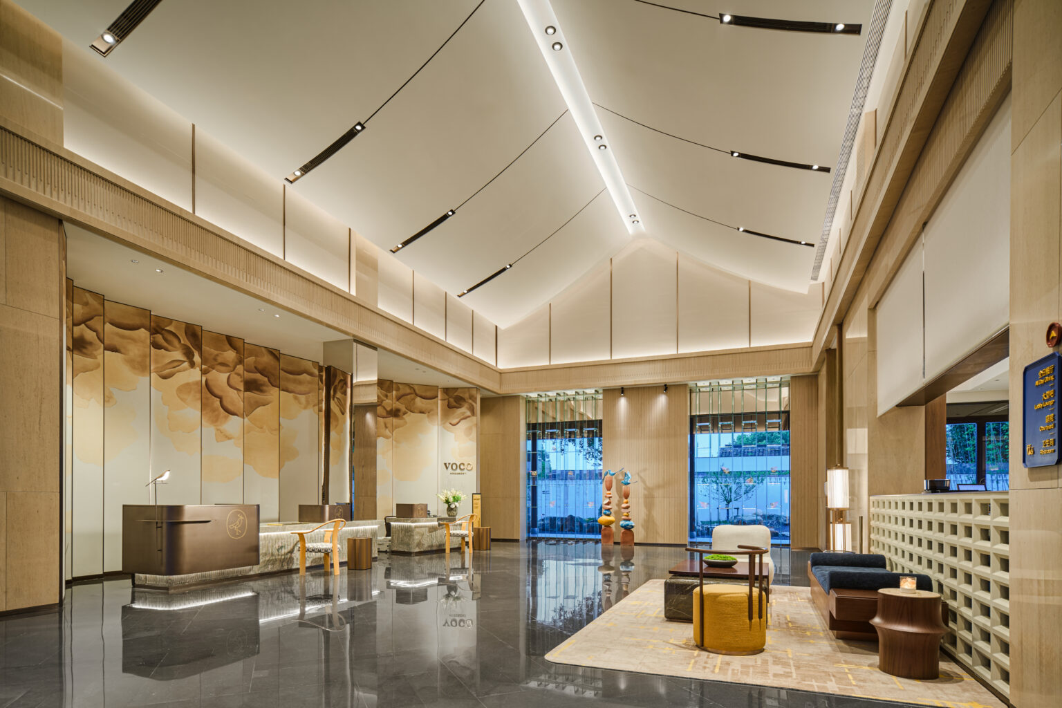 Spacious modern hotel lobby with high ceilings, warm lighting, and elegant decor. Features a reception desk, seating area, and large wall art.