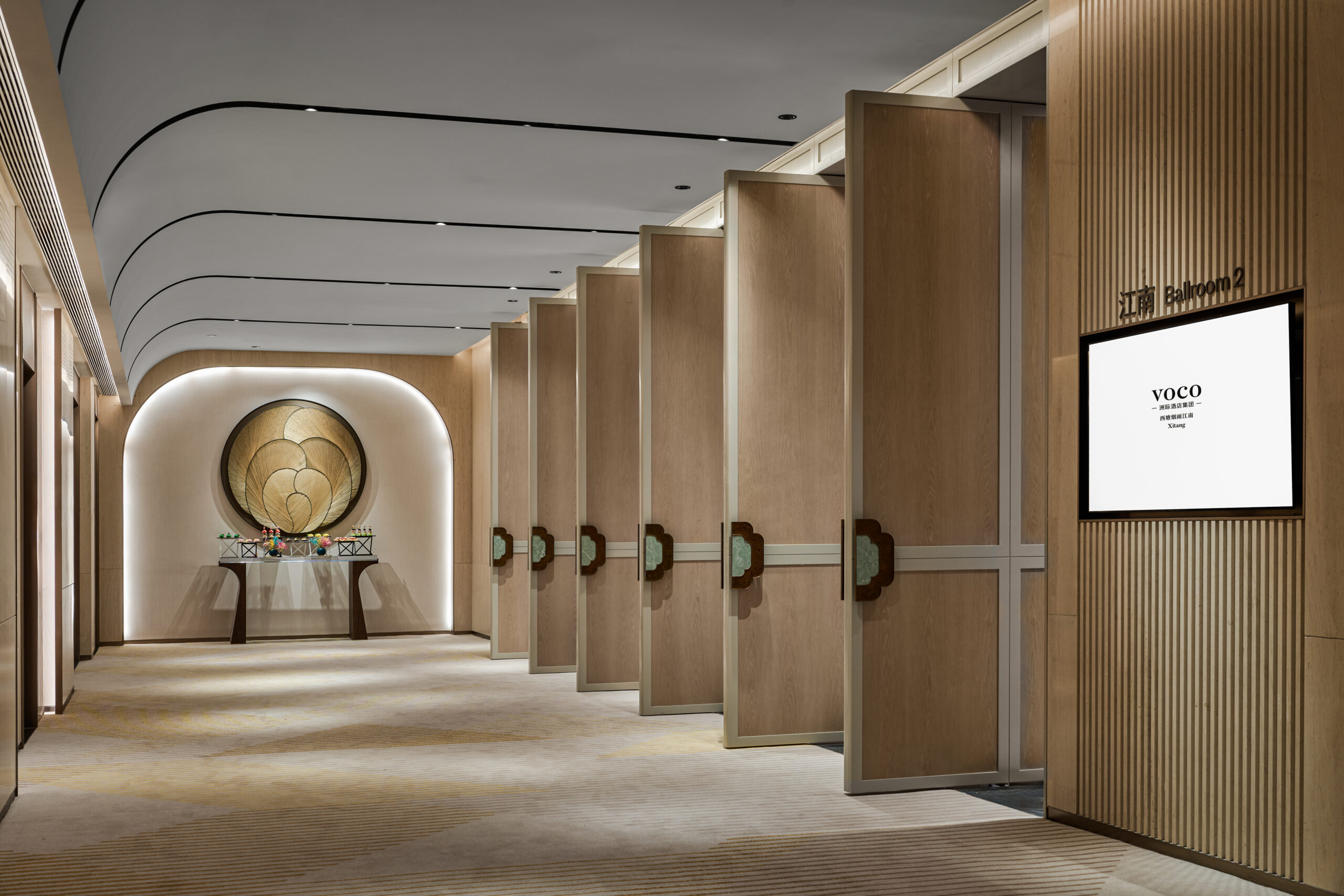 Modern, elegant hallway with wooden paneling and curved ceiling design. Large, open wooden doors line one side. Mood is sophisticated and serene.