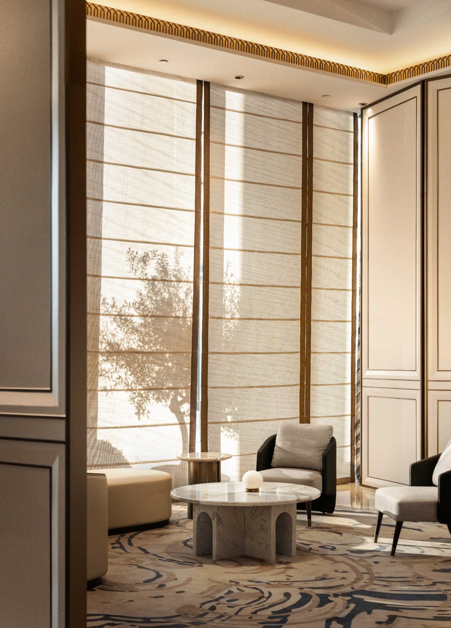 Luxurious lounge with large windows filtered by sheer curtains, casting tree shadows. Features elegant chairs, a stone table, and ornate carpet. Calm ambiance.