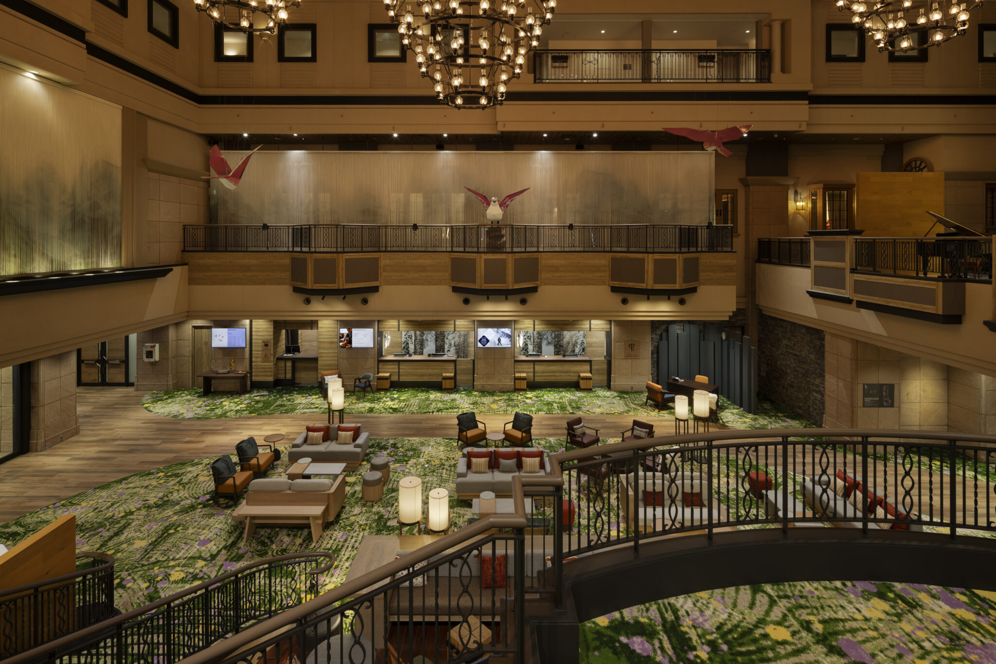 Modern hotel lobby with high ceilings, featuring a central tall tree, elegant seating, a stylish bar with hanging lights, and a serene ambience.