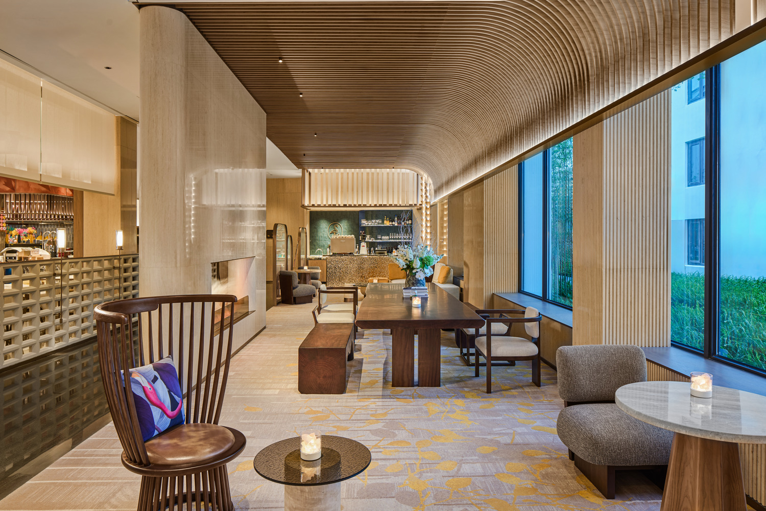 Modern lobby bar with wooden ceiling and elegant furniture, including a high-backed chair, table, and sofa. Soft lighting creates a warm, inviting atmosphere.