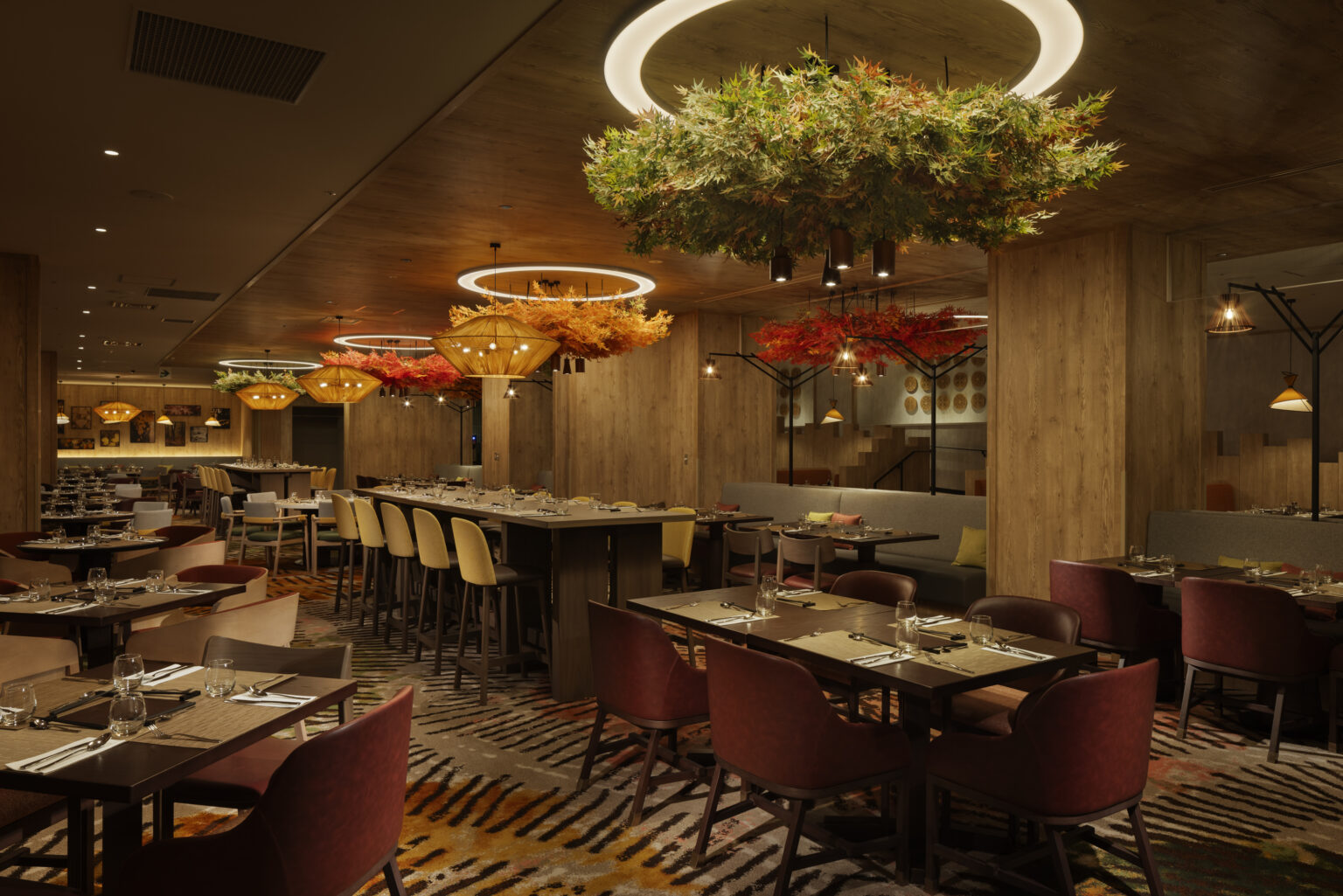 Elegant restaurant interior with dim lighting, patterned carpet, and tables set for dining. Decorative, leafy chandeliers create a warm, inviting atmosphere.
