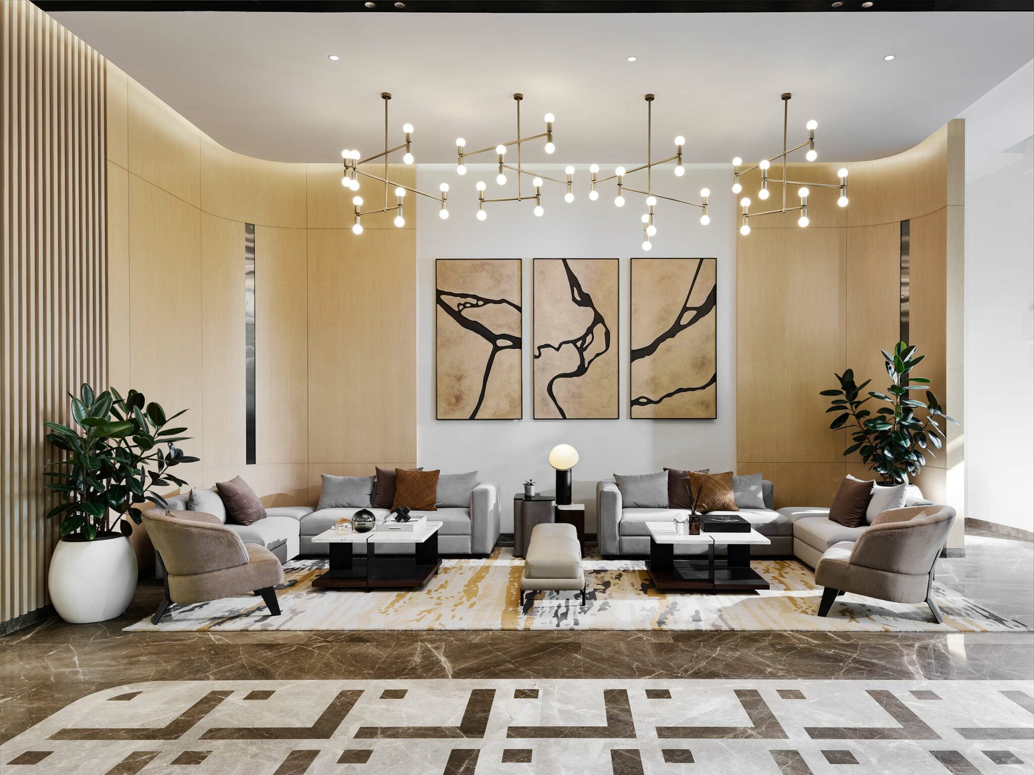 Modern lobby with a warm tone, featuring neutral sofas, abstract triptych art, sleek chandeliers, potted plants, and a geometric patterned carpet.
