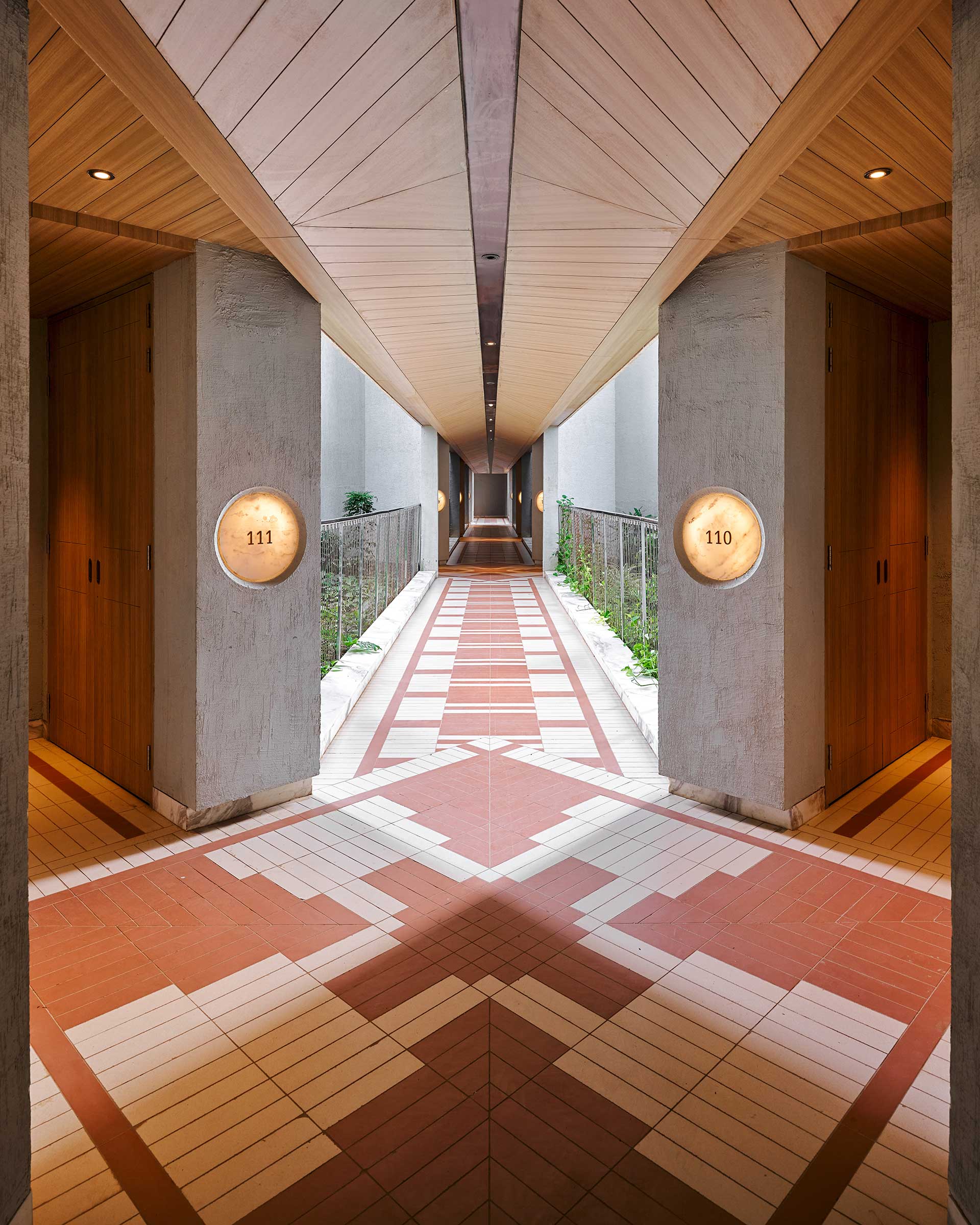 A modern hallway with geometric tiled flooring in red and white, flanked by two wooden doors labeled 110 and 111. The space feels sleek and minimalist.