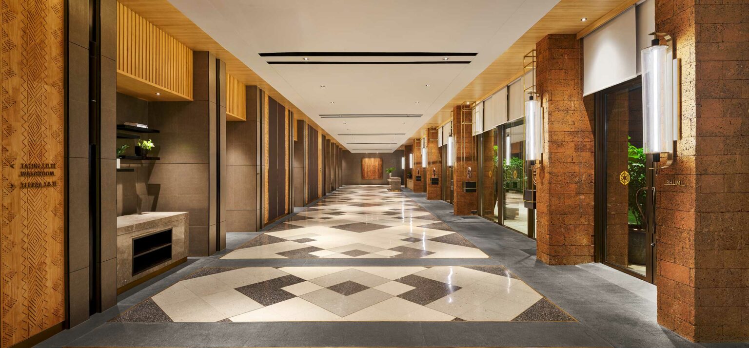Spacious hotel lobby with a modern design, featuring geometric patterned flooring, wooden accents, soft lighting, and a calm, inviting atmosphere.