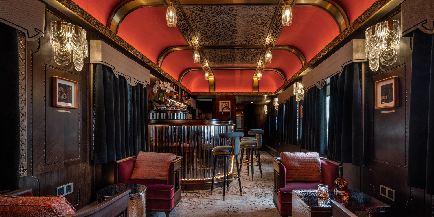 Luxurious train carriage bar with a vintage feel, featuring red and gold arched ceiling, plush seating, chandeliers, and a polished counter. Cozy and elegant ambiance.