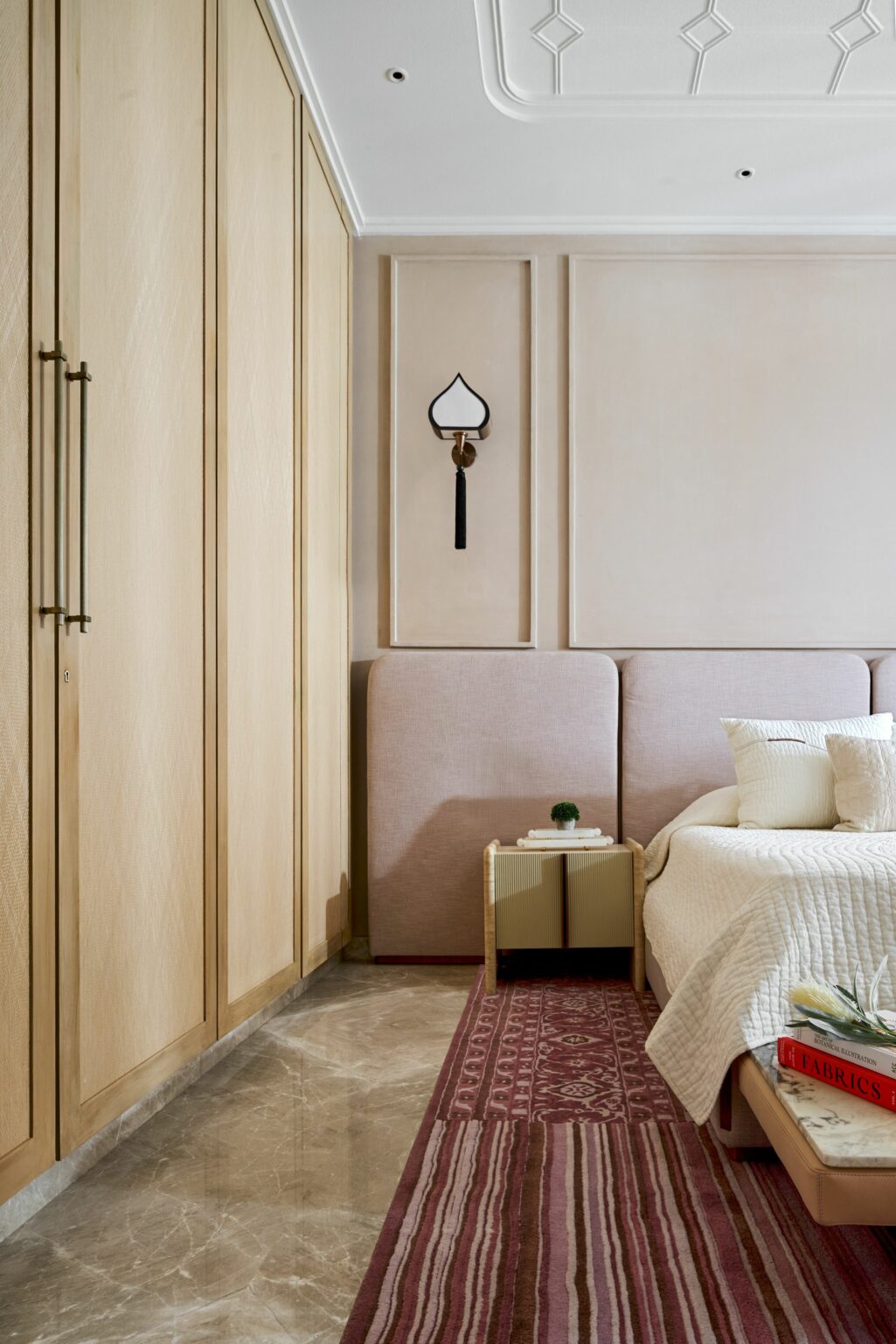 Modern bedroom with light wood paneling, pink upholstered bed, and white bedding. A small side table and patterned rug add warmth and texture.