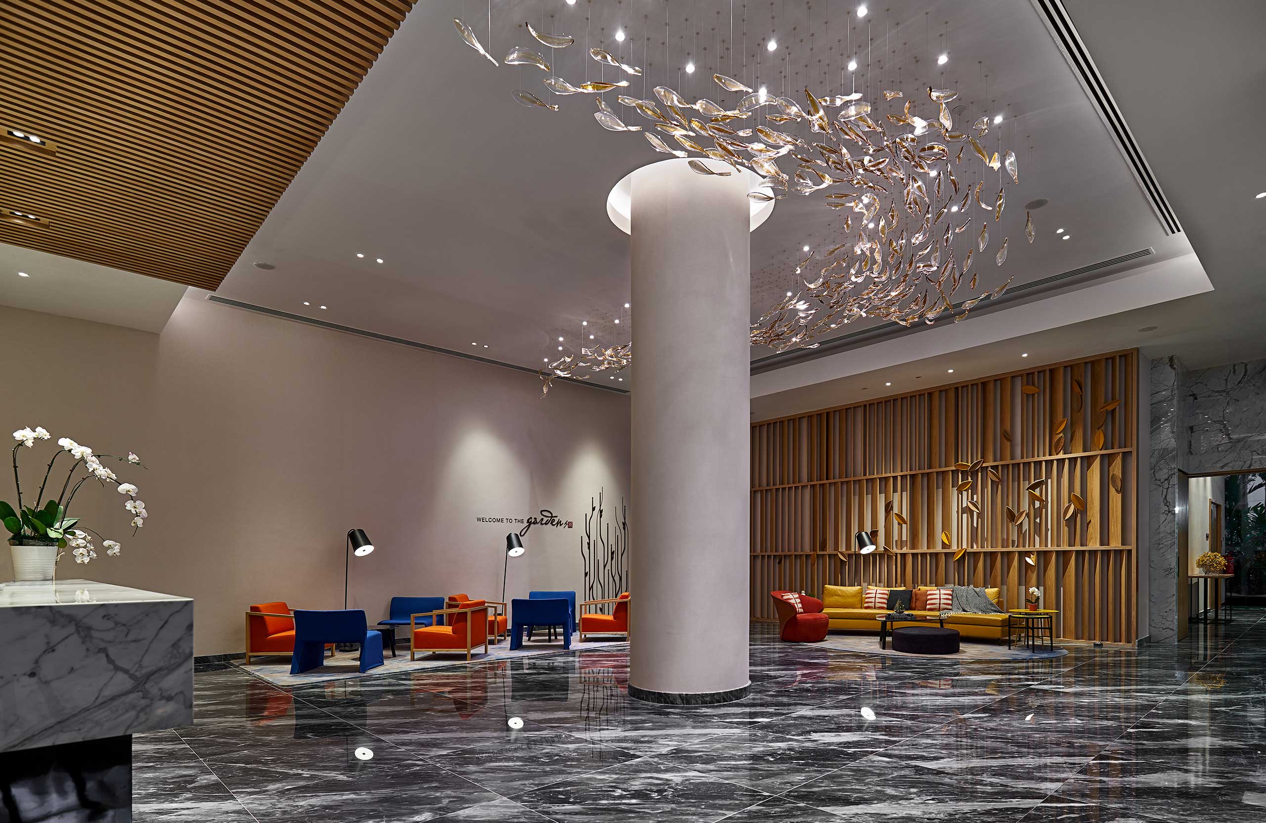 Modern hotel lobby with gleaming marble floor, colorful seating areas, and a central pillar. Decorative ceiling art adds elegance and luxury.