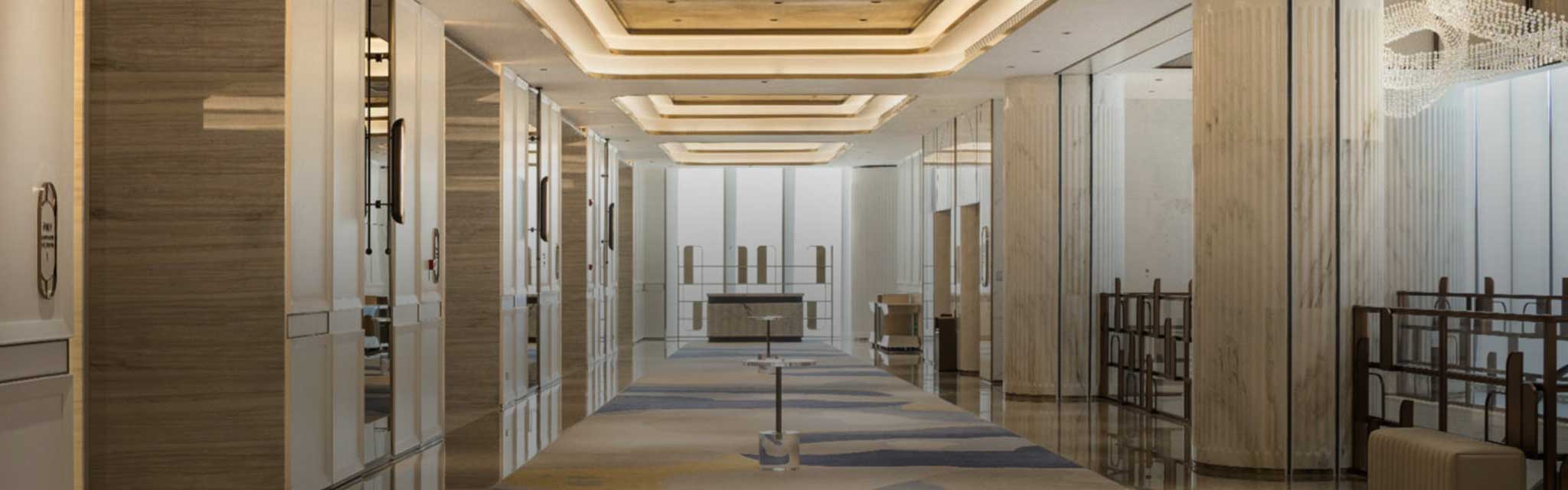 Luxurious hotel lobby with elegant lighting, polished floors, and modern decor. Soft, neutral tones and symmetrical design create a serene atmosphere.