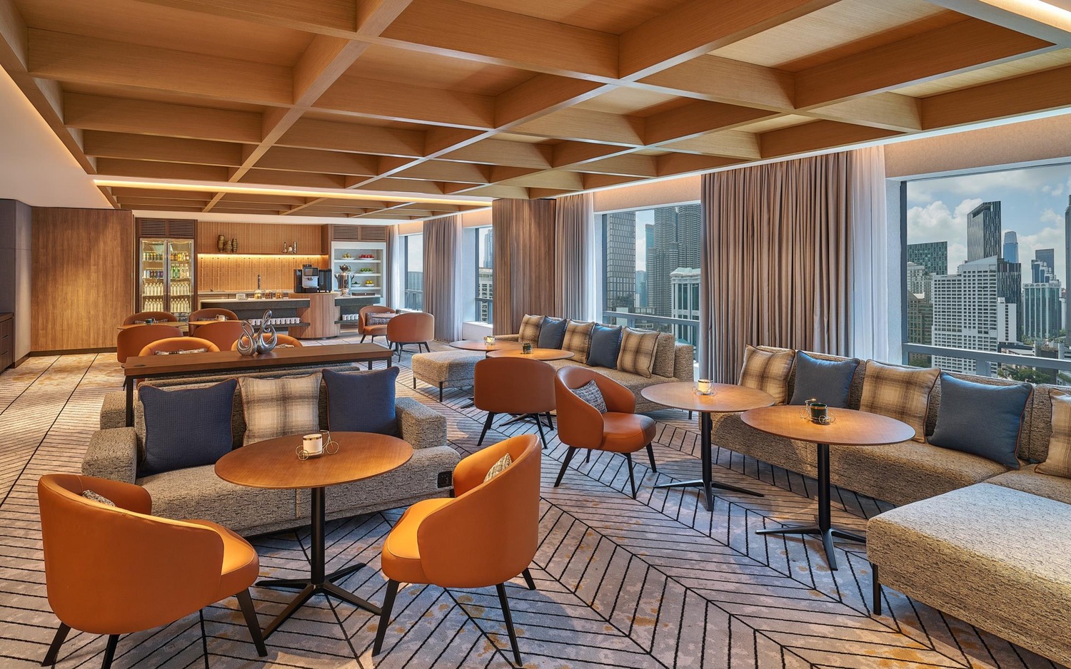 Sophisticated lounge with modern decor, featuring gray sofas, orange chairs, wooden tables, large windows with city views, and a cozy ambiance.