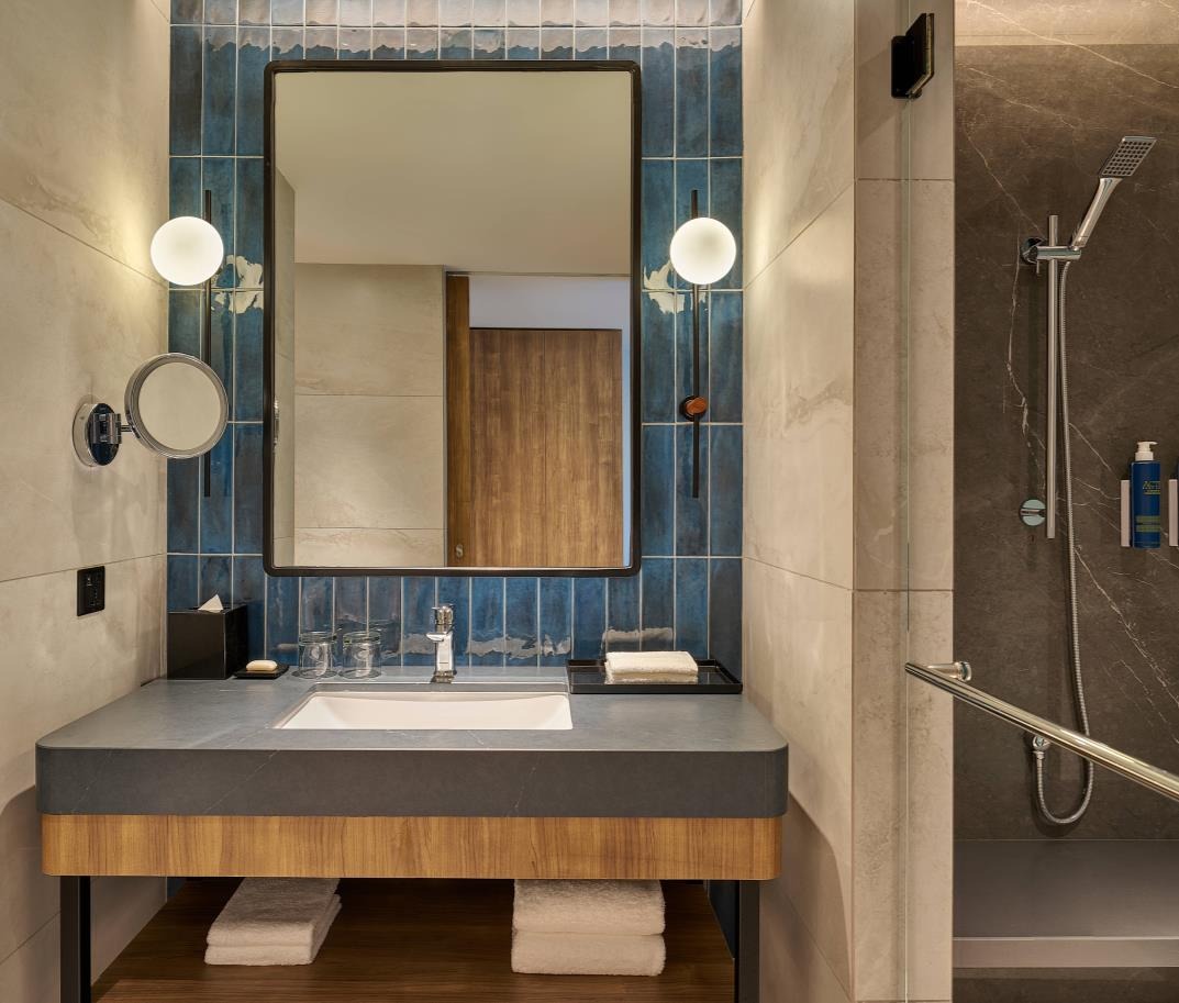 Modern bathroom with a sleek vanity, rectangular mirror, and blue-tiled backsplash. Stylish lighting and a walk-in shower create a clean, tranquil ambiance.